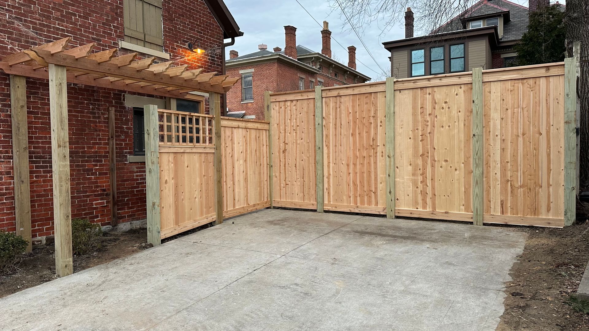 A wooden fence is surrounding a driveway in front of a brick house.