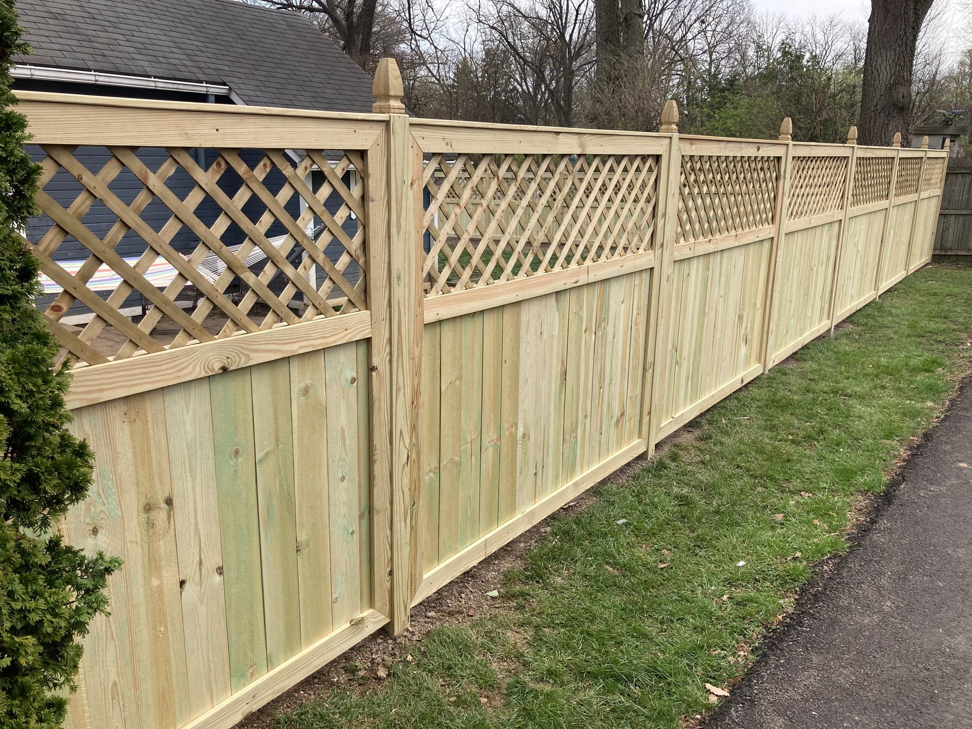 A wooden fence with a lattice design is sitting next to a road.