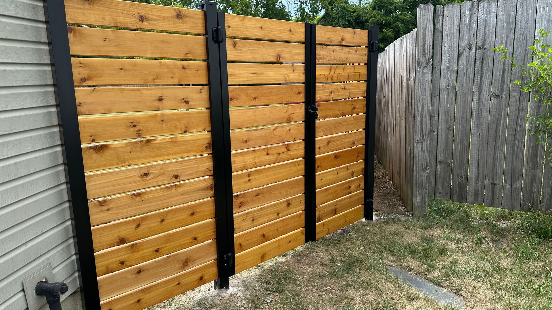 A wooden fence with black trim is in the backyard of a house.