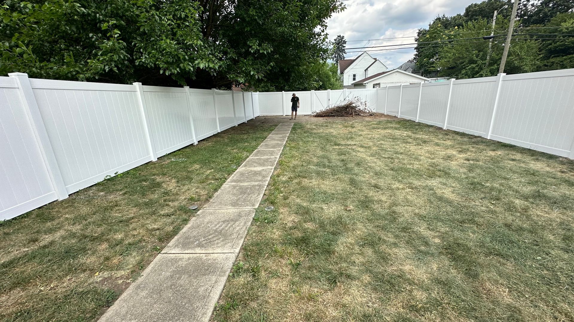 A white fence surrounds a lush green yard with a sidewalk leading to it.