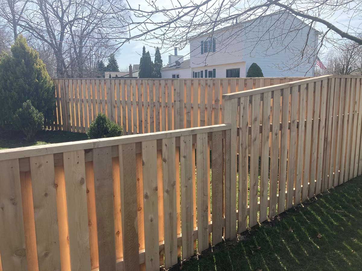 A wooden fence in a backyard with a house in the background.