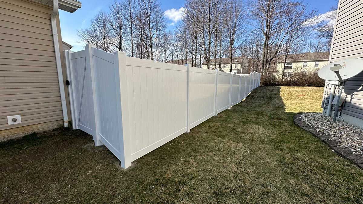 A white vinyl fence is in the backyard of a house.