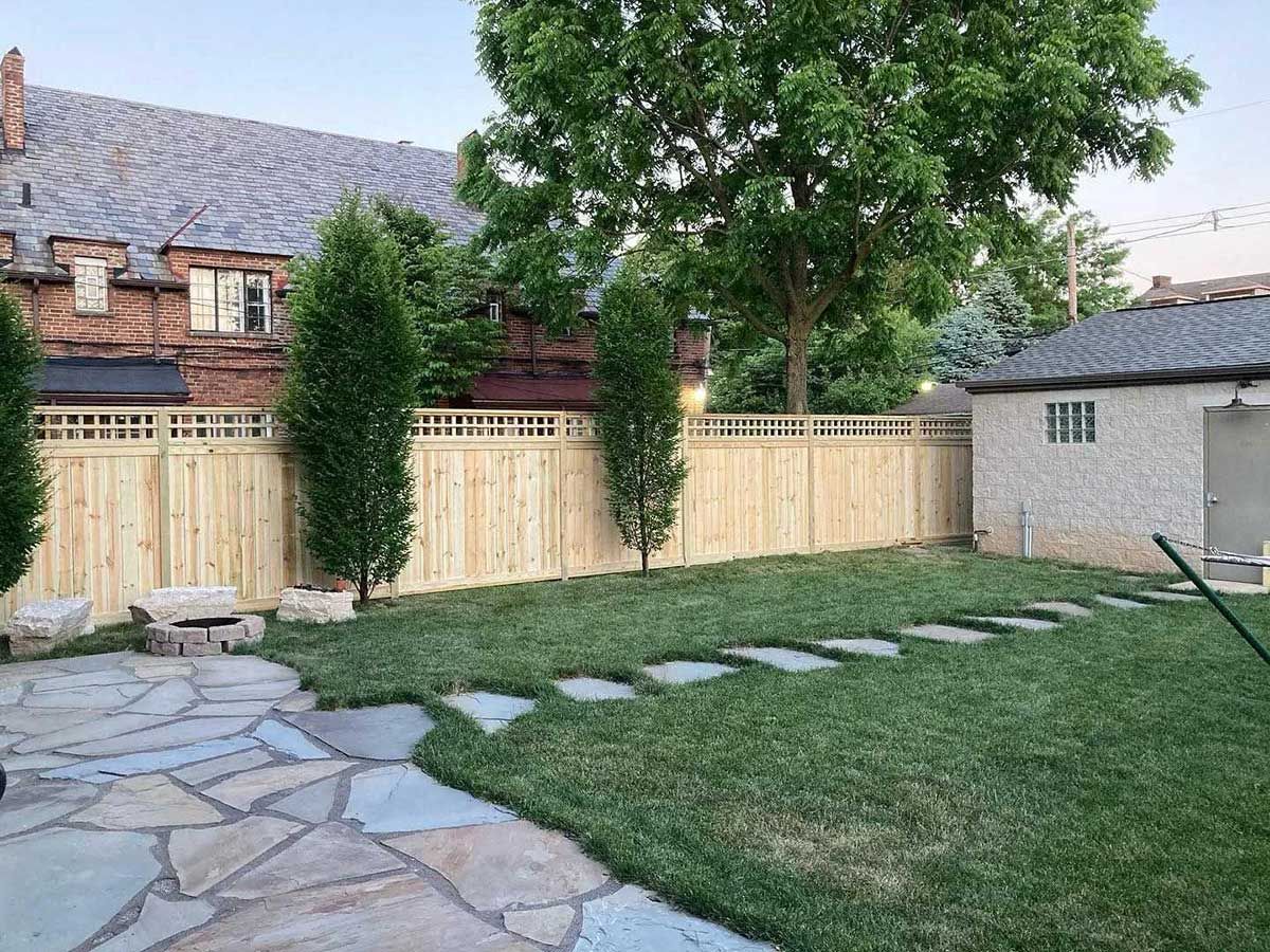 A backyard with a wooden fence and a stone walkway.