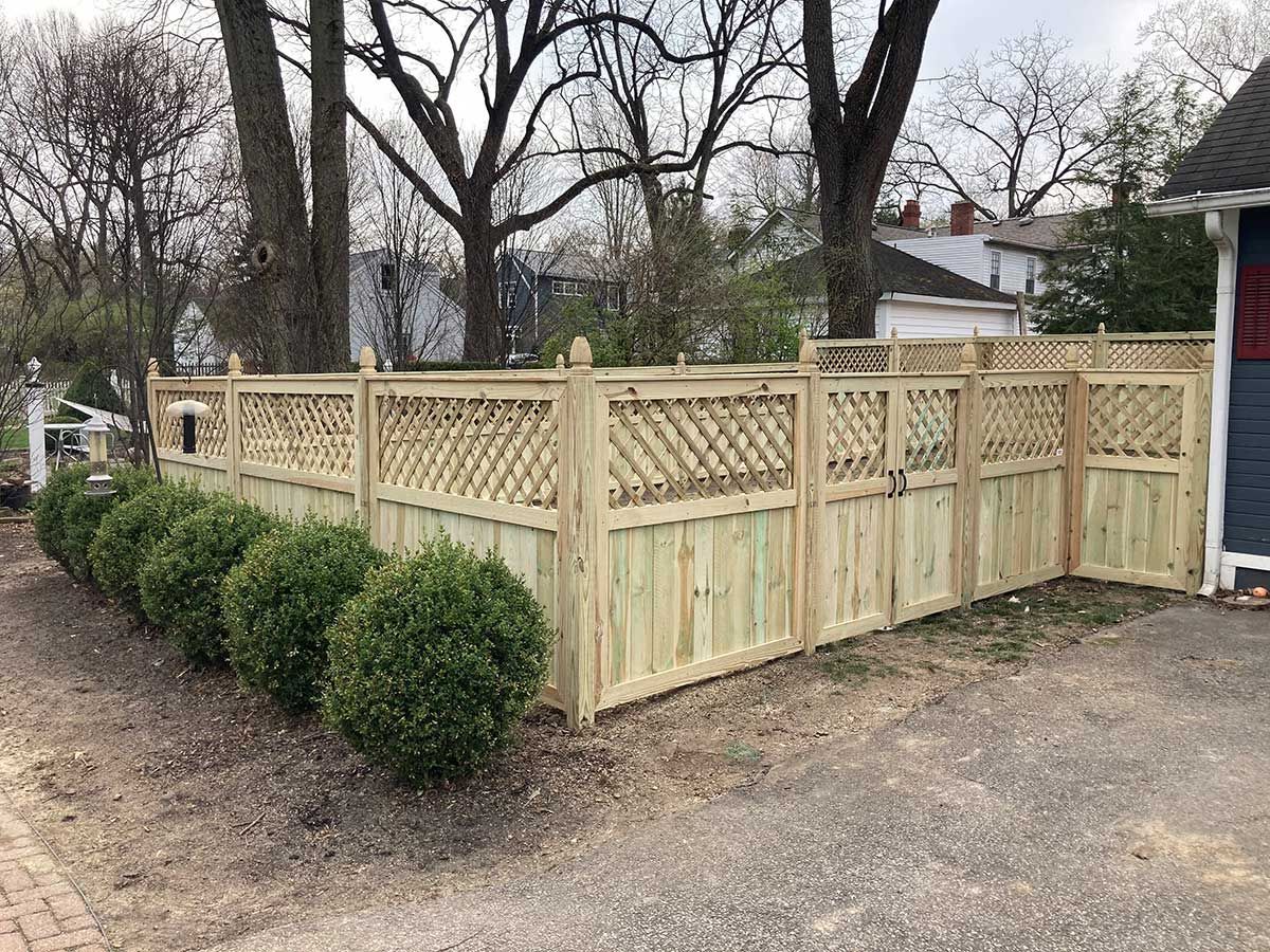 A wooden fence is surrounded by bushes and trees in front of a house.