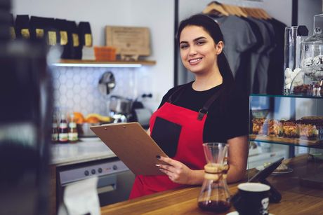 A woman is standing at a counter in a restaurant holding a clipboard.