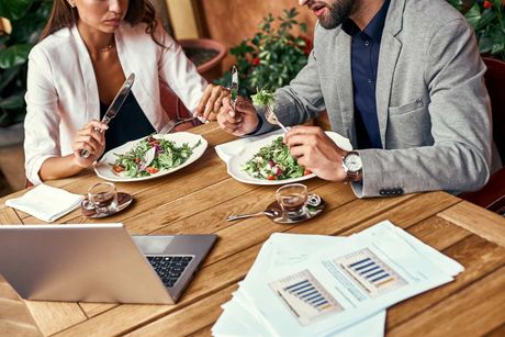 A man and a woman are sitting at a table eating salad.