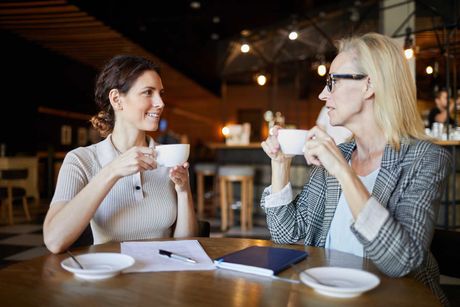 Two women are sitting at a table drinking coffee.