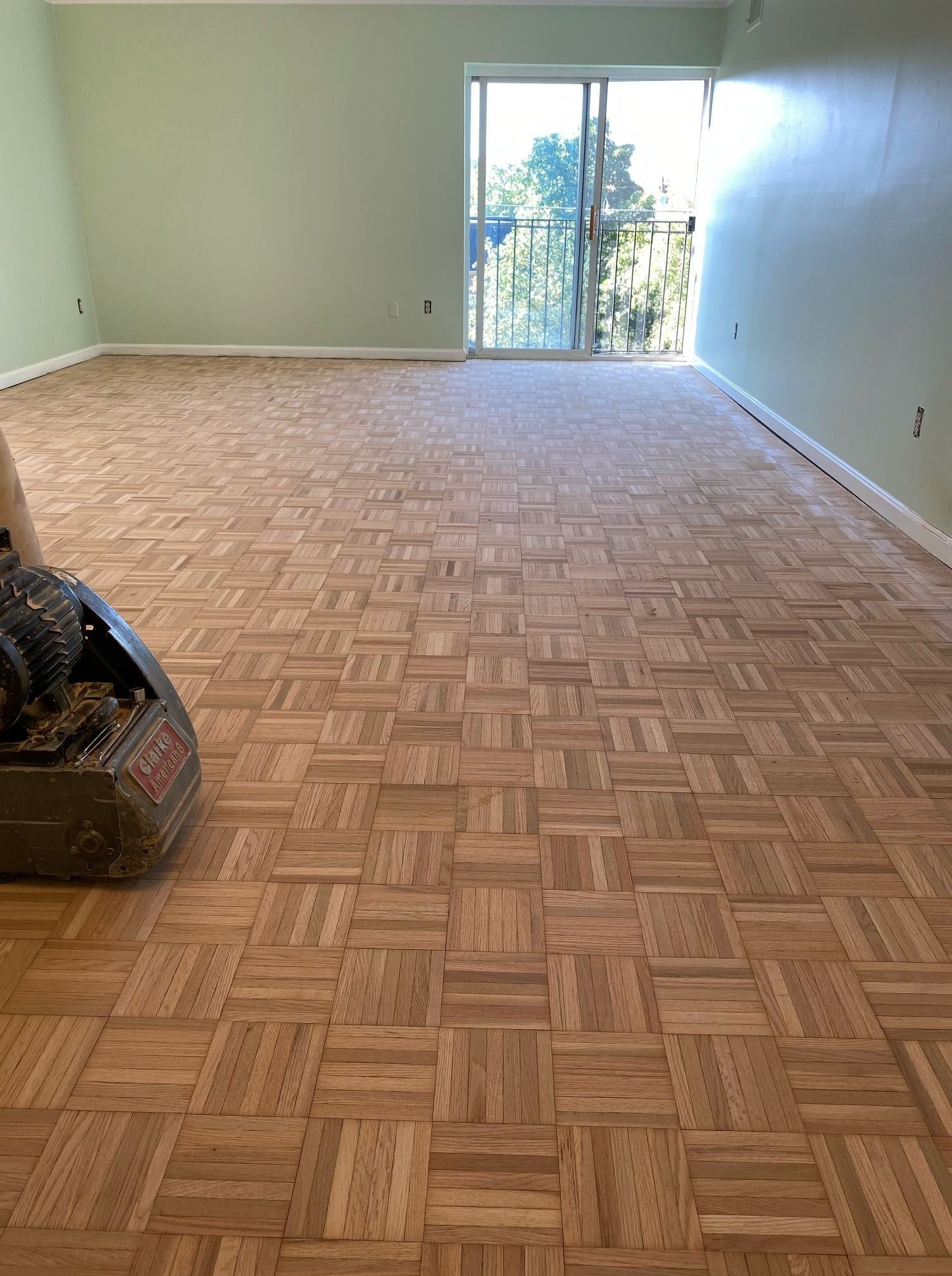A person is sanding a wooden floor in a living room.
