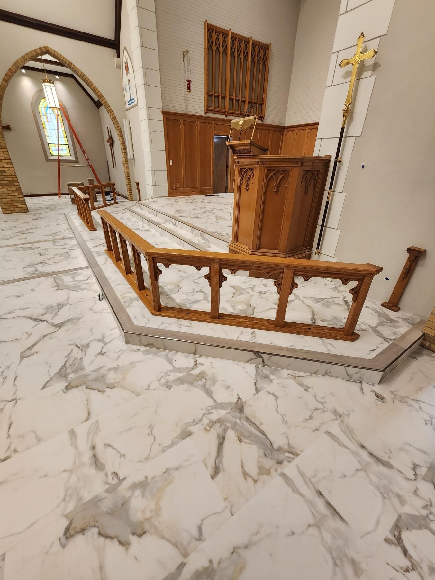 Church interior with marble floor, wooden altar, and railing. Stained glass window in background.