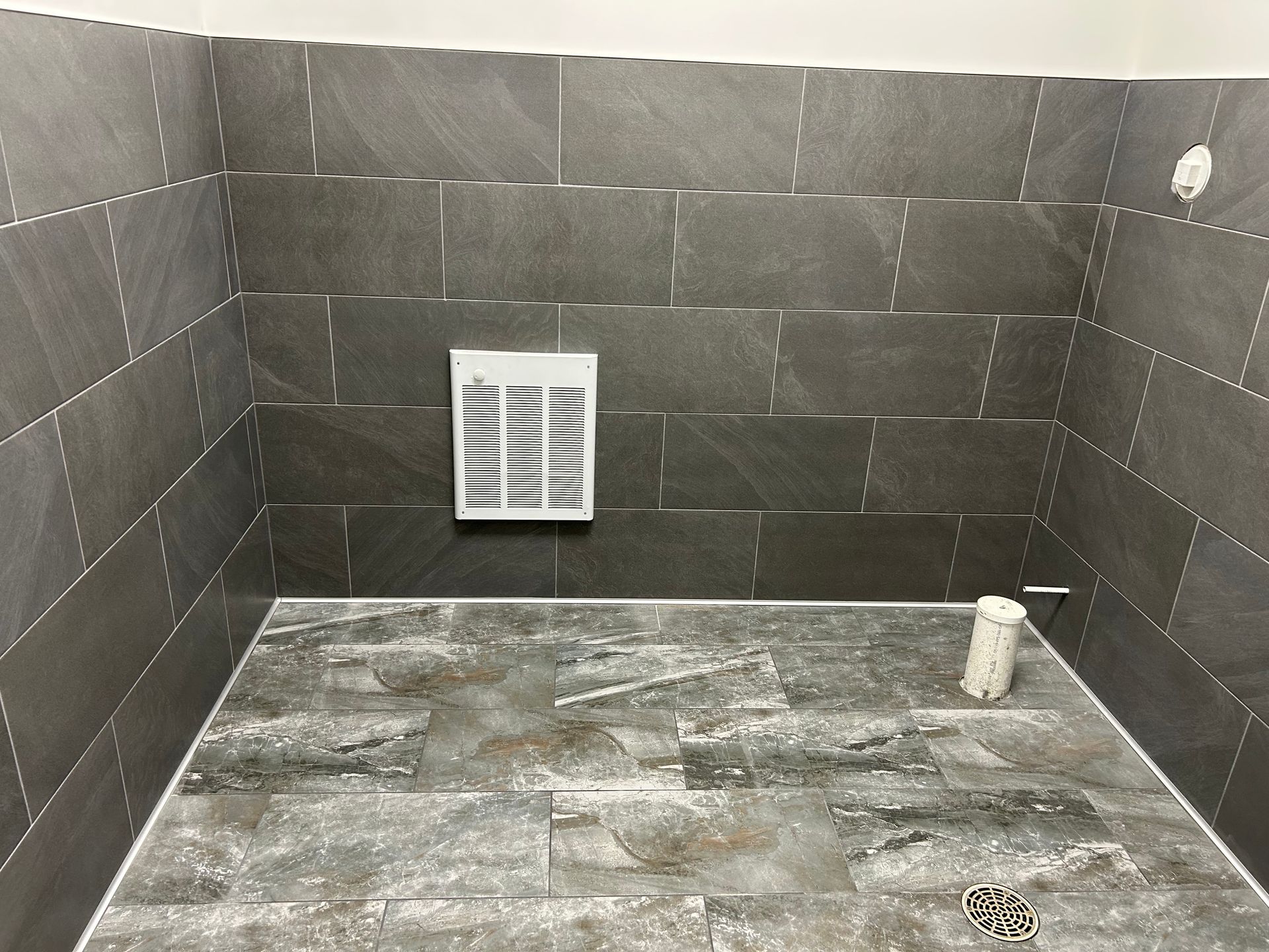 Gray tiled shower stall with a ventilation fan and a water pipe.