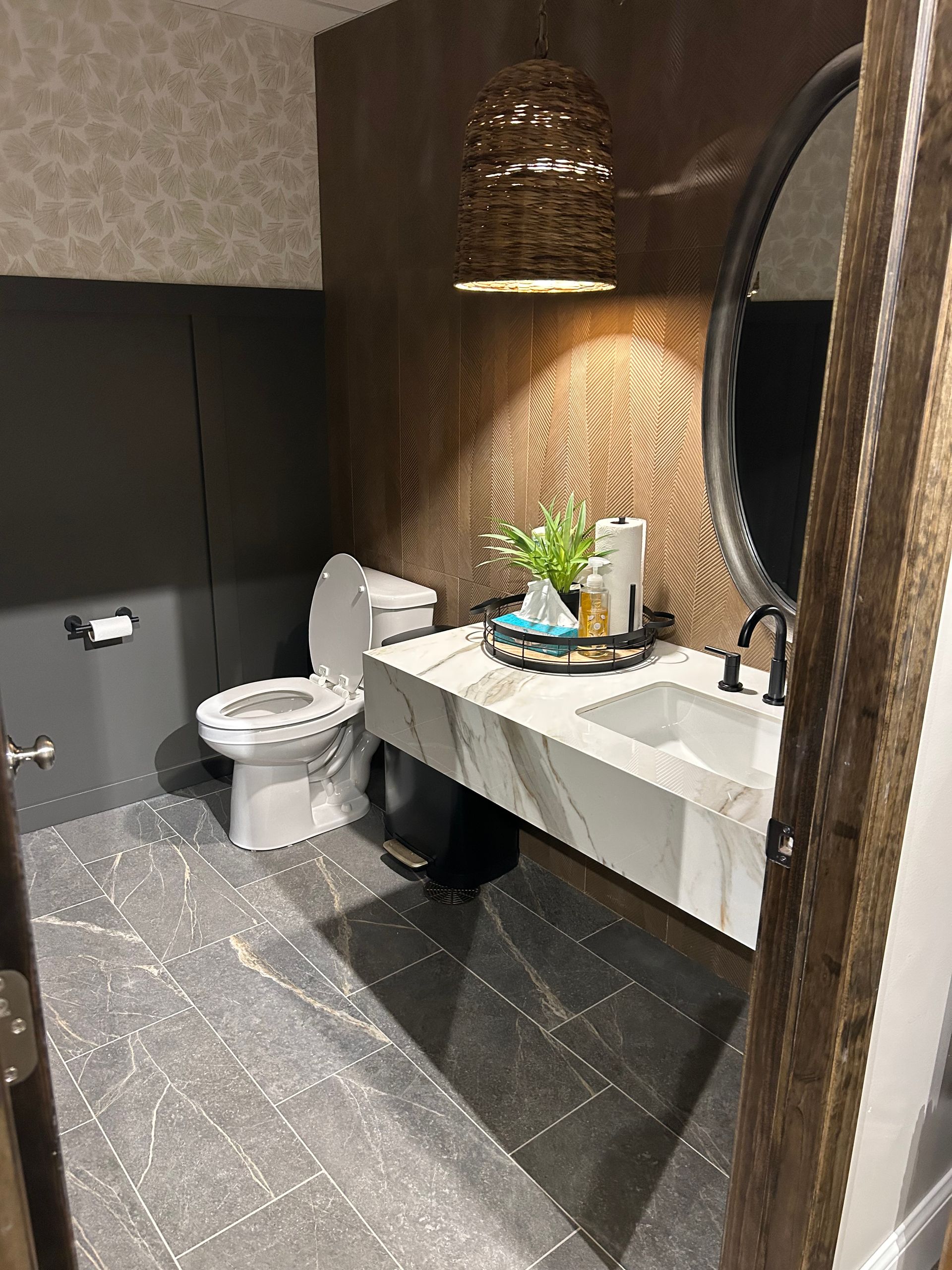 A bathroom with a floating marble sink, toilet, textured wallpaper, and gray tiled floor.