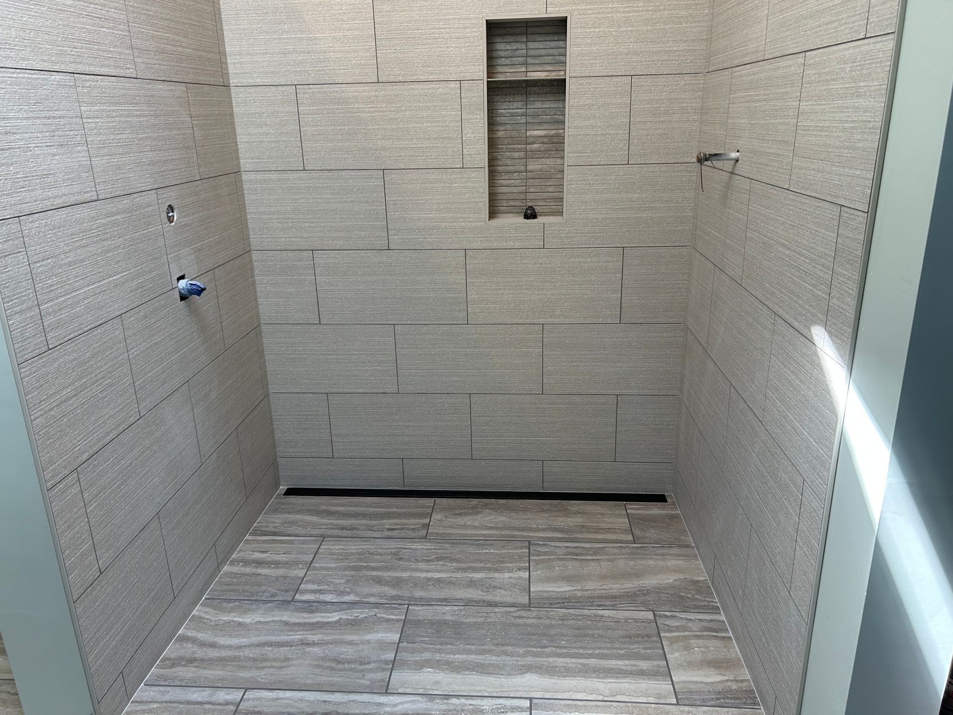 Empty shower with beige tiled walls and floor, built-in shelf, and black drain.