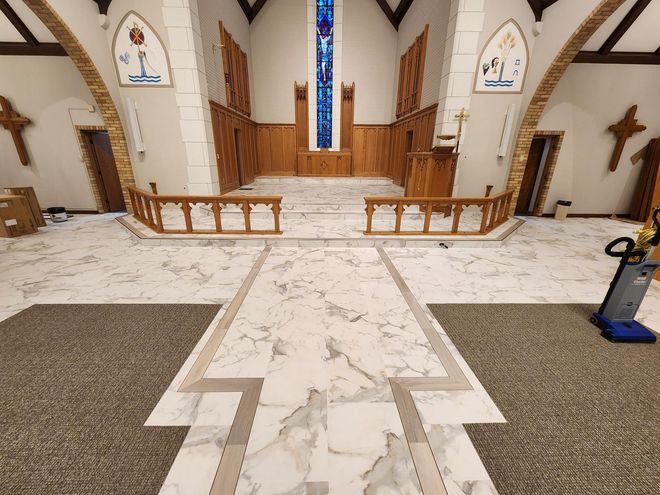 Interior of a church with marble and carpet flooring, wooden features, and a stained-glass window.