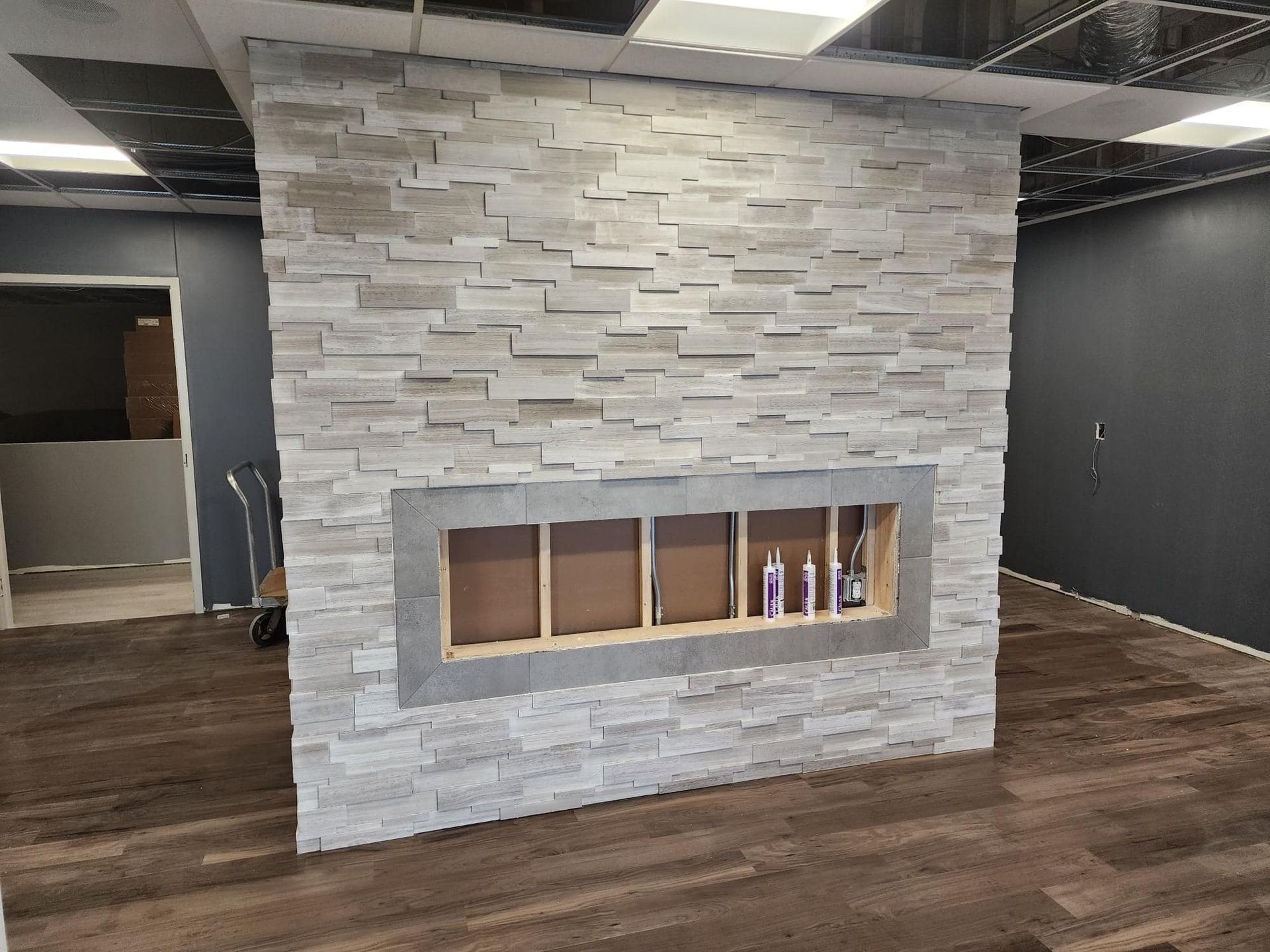 Stone accent wall with rectangular opening; wood-look flooring. Dark gray wall and open doorway visible.