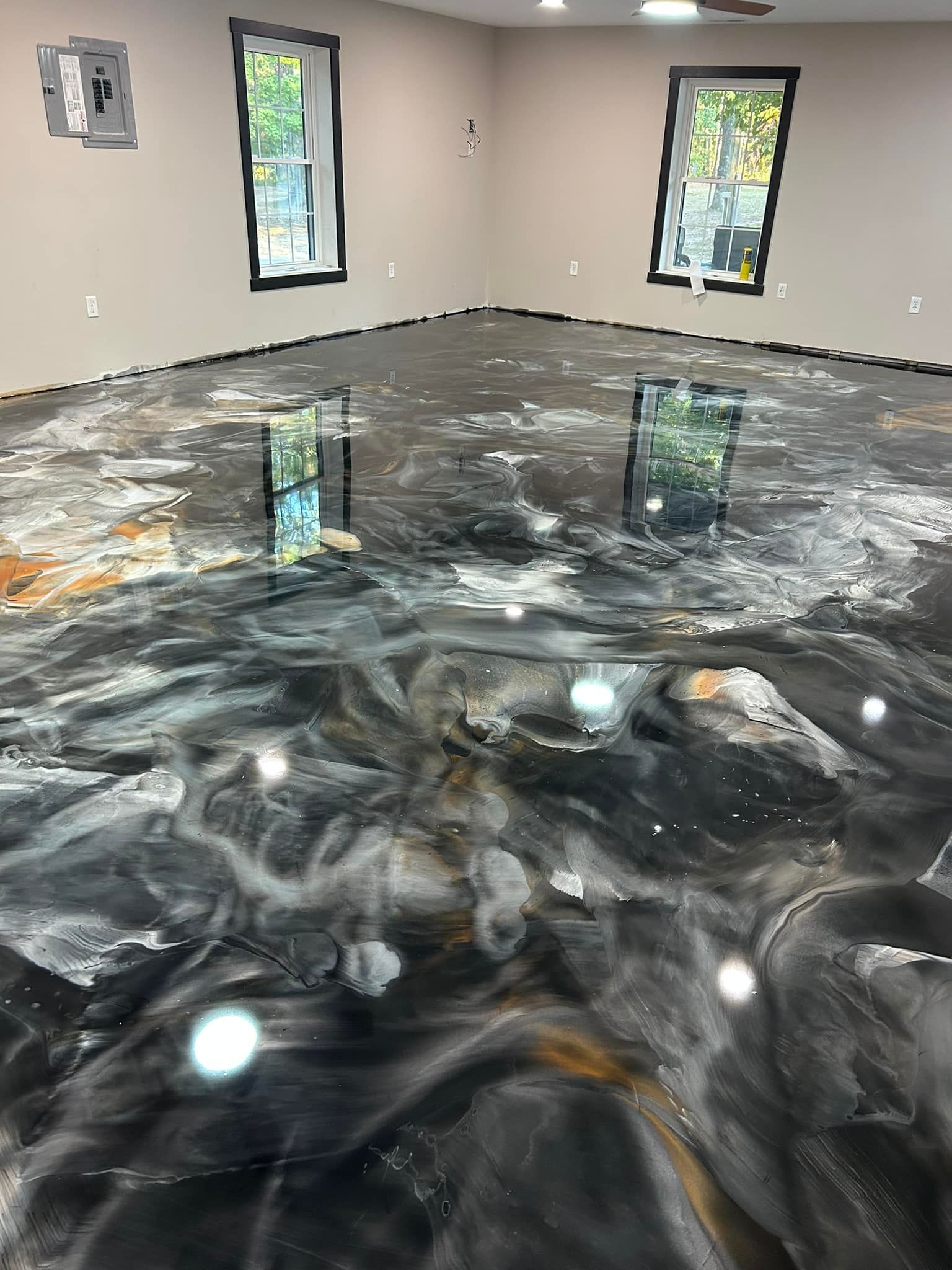 Epoxy floor with black, white, and gold swirls in a room with two windows and beige walls.