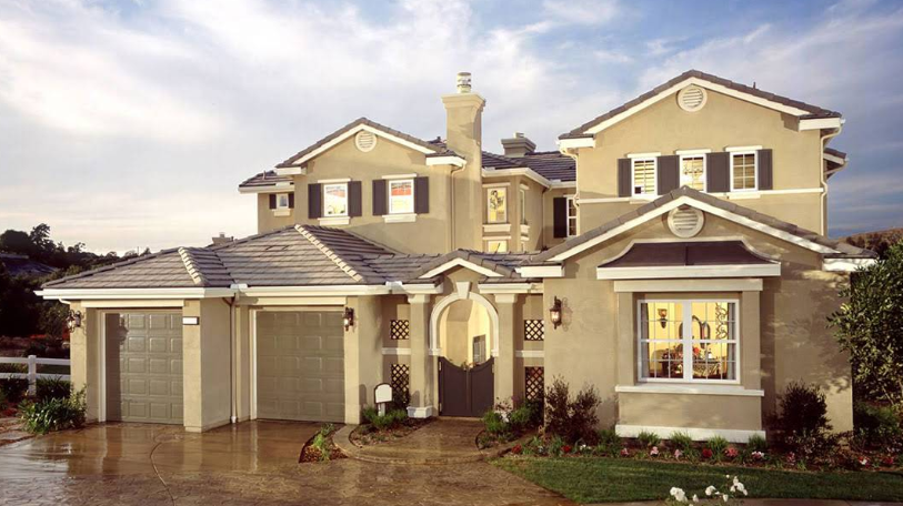 Two-story beige stucco house with a garage, shutters, and a front archway.
