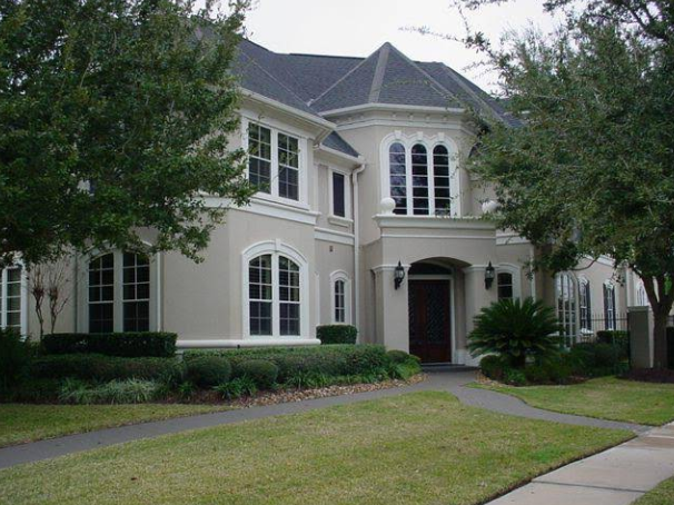 Two-story beige house with dark roof and landscaping, pathway to front door.