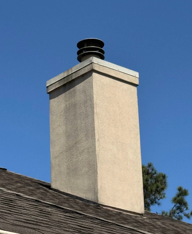 Tall, rectangular chimney with a metal cap on a roof against a blue sky.