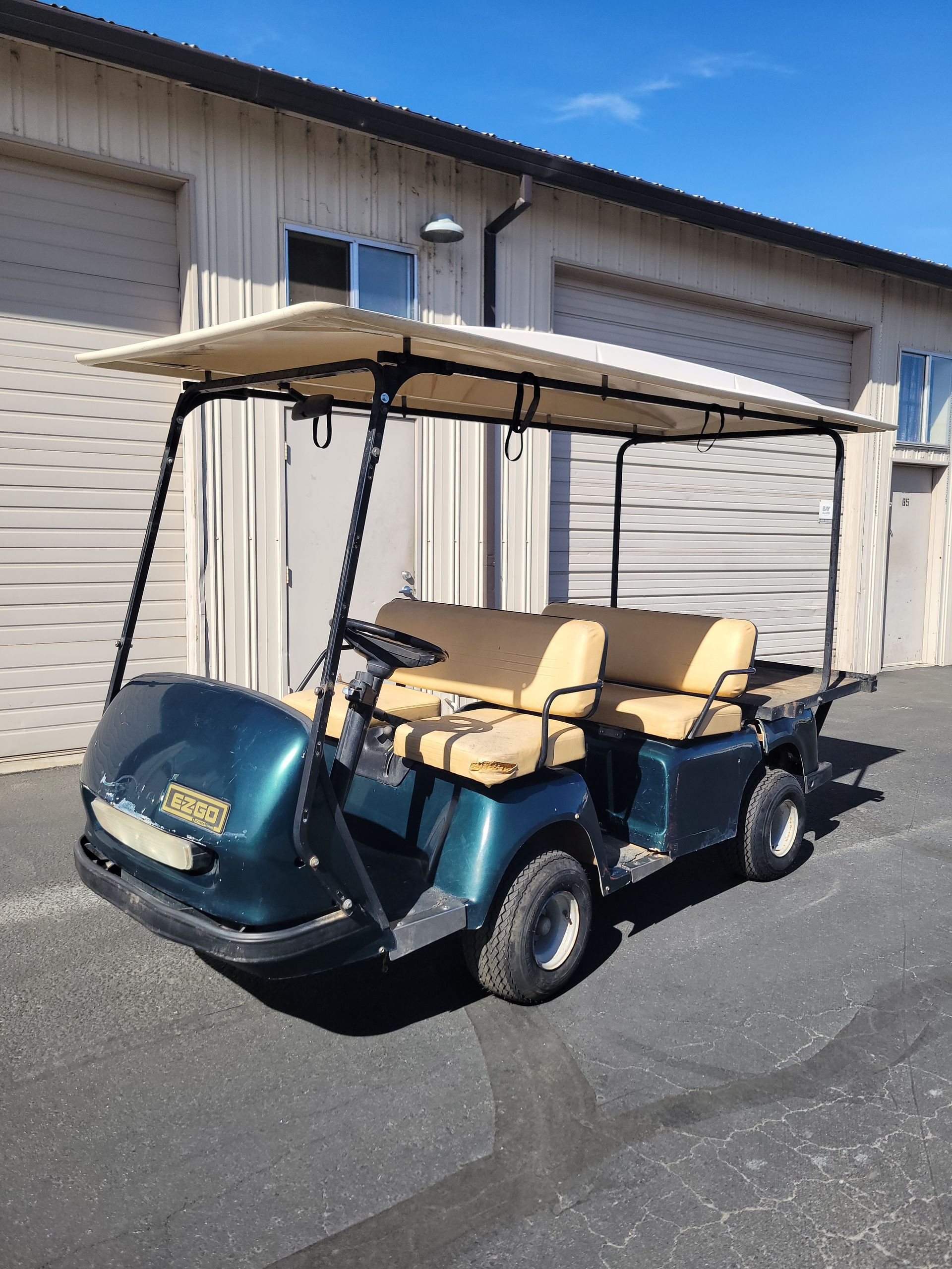 Golf cart with beige seats and canopy parked outside a white industrial building.
