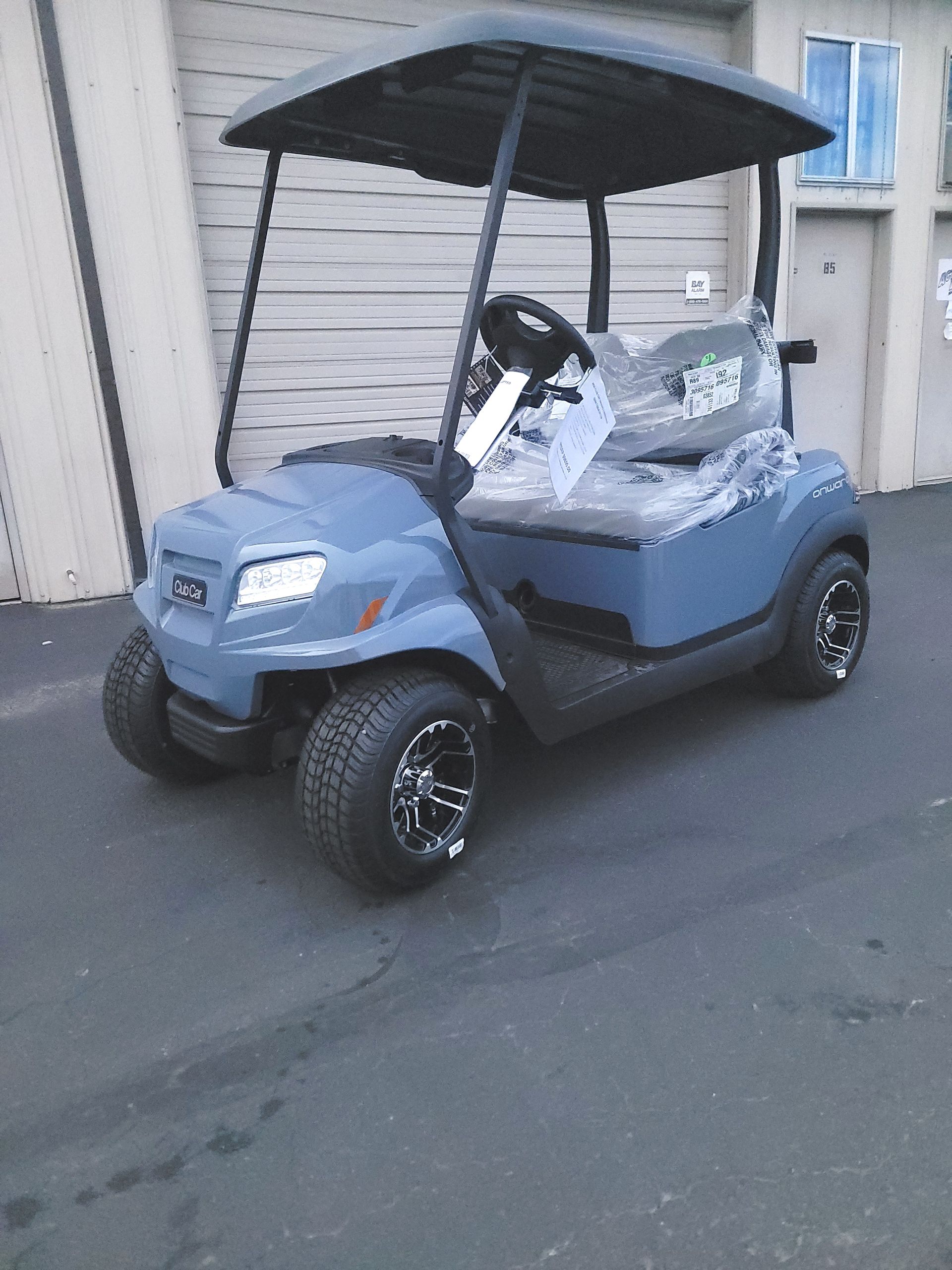 Blue Club Car golf cart with black roof and wheels parked on asphalt.