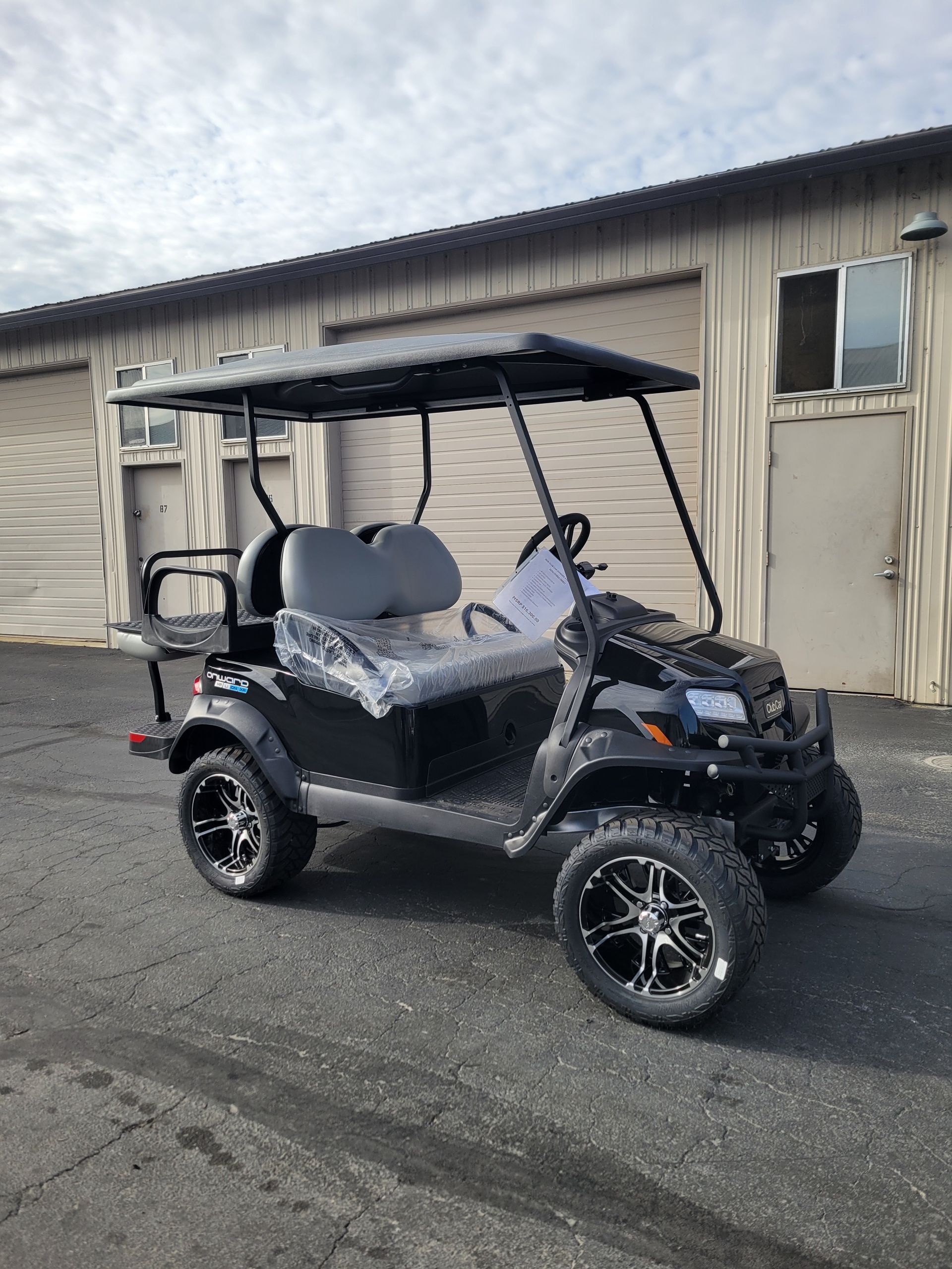 Black golf cart with lifted suspension and custom wheels parked outside a warehouse.