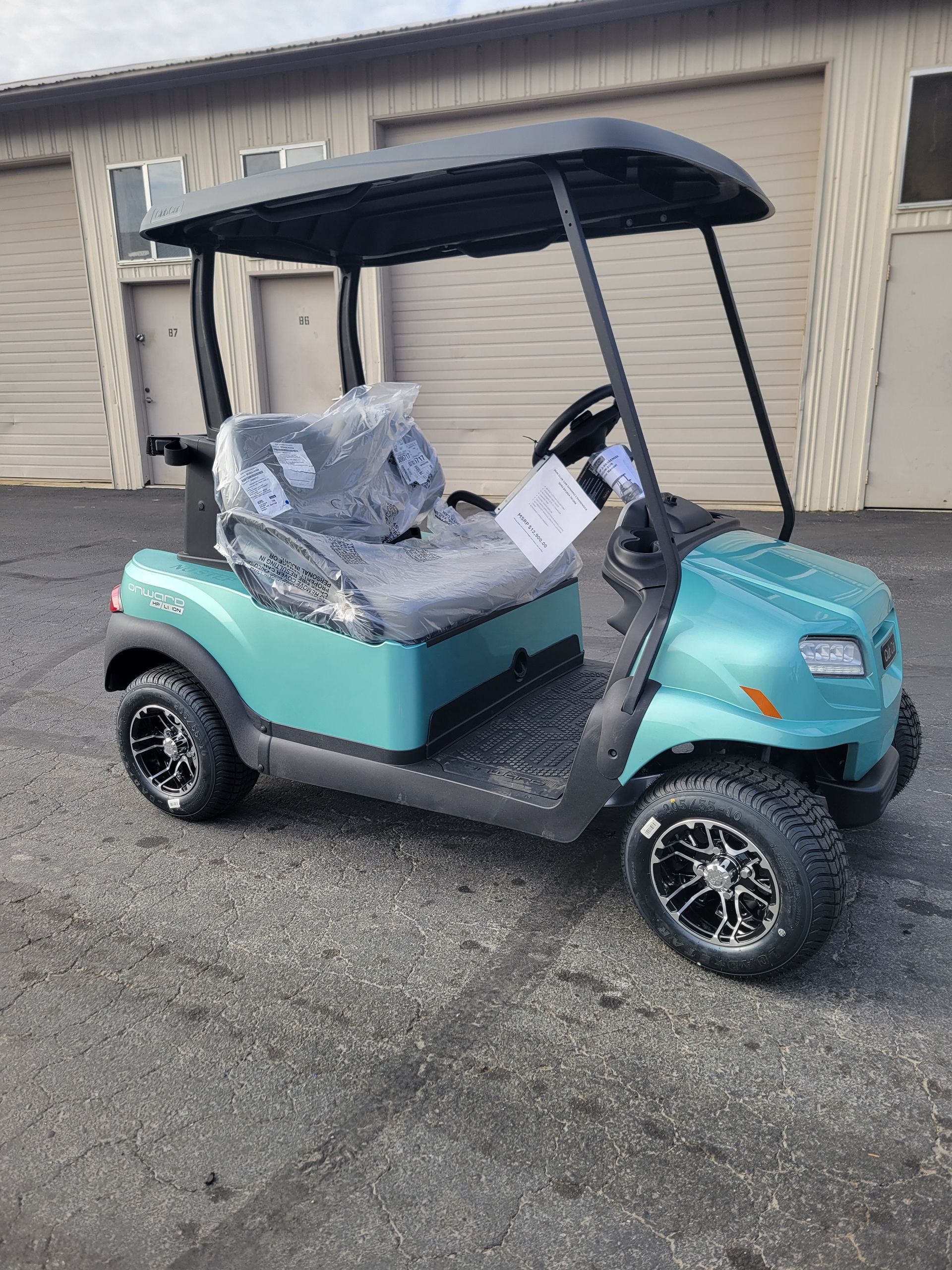 Teal golf cart with black roof and wheels parked outside a tan building.