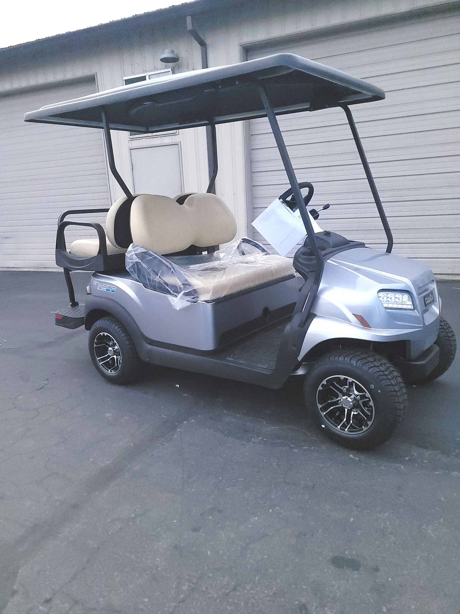 Gray golf cart with black roof and wheels, parked outside a building.