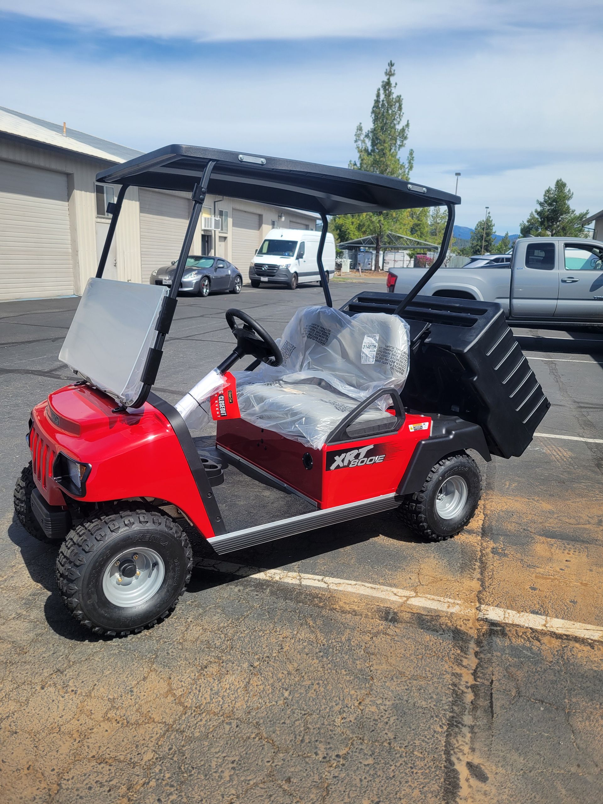 Red golf cart with black canopy and seats parked on pavement beside a building.