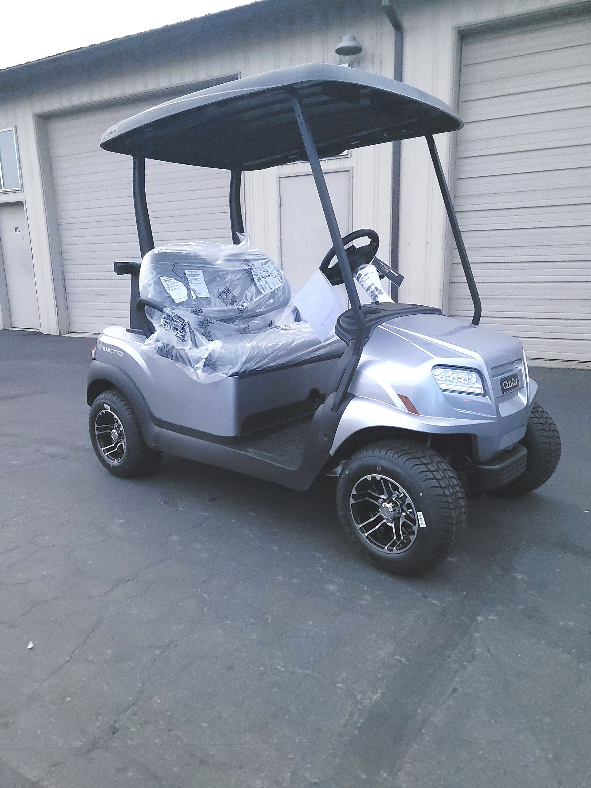 Gray golf cart parked in front of garage doors. Black roof and wheels.
