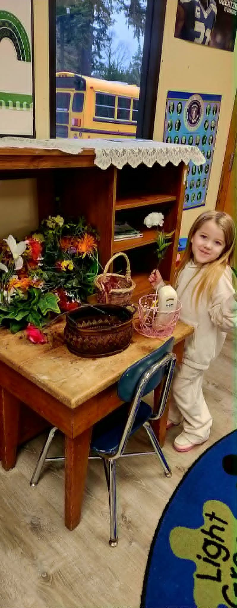 Child standing beside a wooden table with flowers and a basket in a cozy playroom