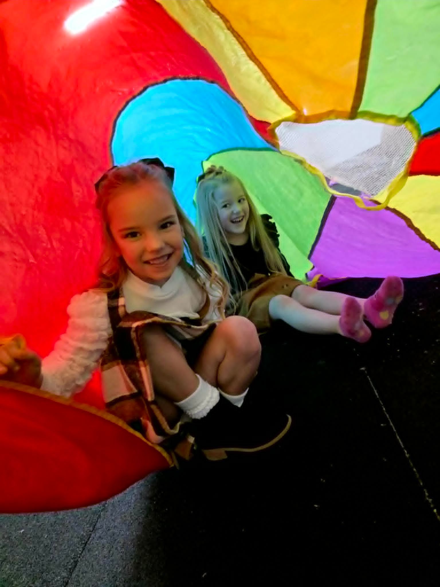 Two children sitting inside a colorful translucent play tunnel, smiling at the camera.