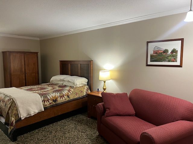 A bedroom with a bed, couch, lamp, and picture on the wall.