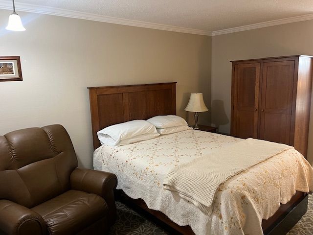 A bedroom with a bed, chair, and lamp