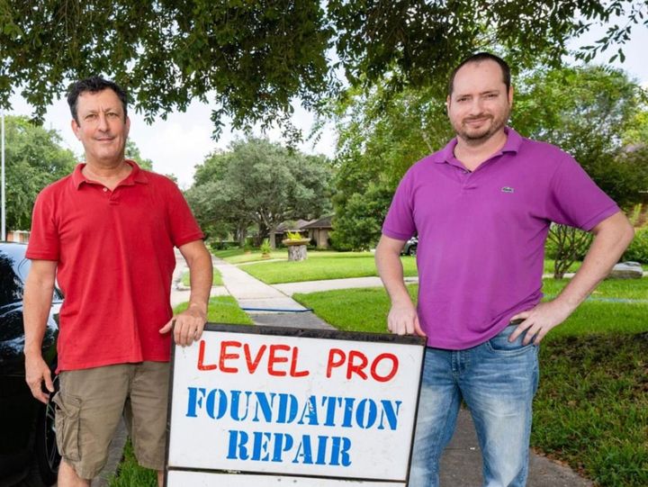 Two men standing by a yard sign reading “Level Pro Foundation Repair,” in a grassy suburban setting.