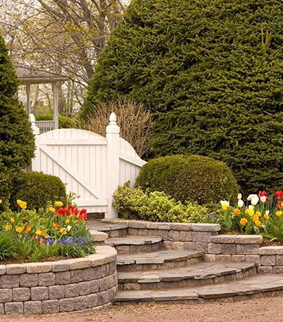 A garden with stairs and flowers and a white fence