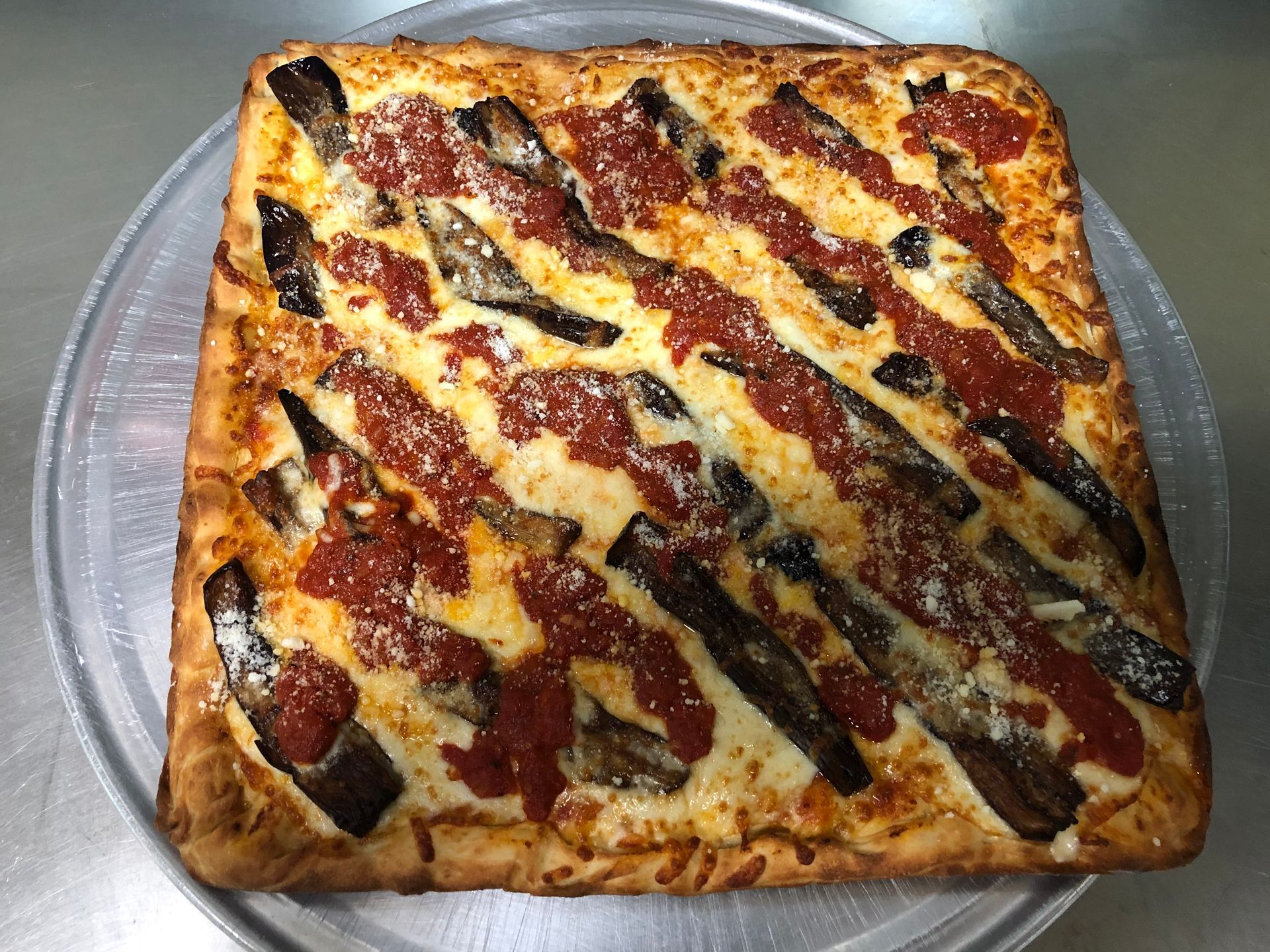 a square pizza with eggplant and tomato sauce on a pizza pan