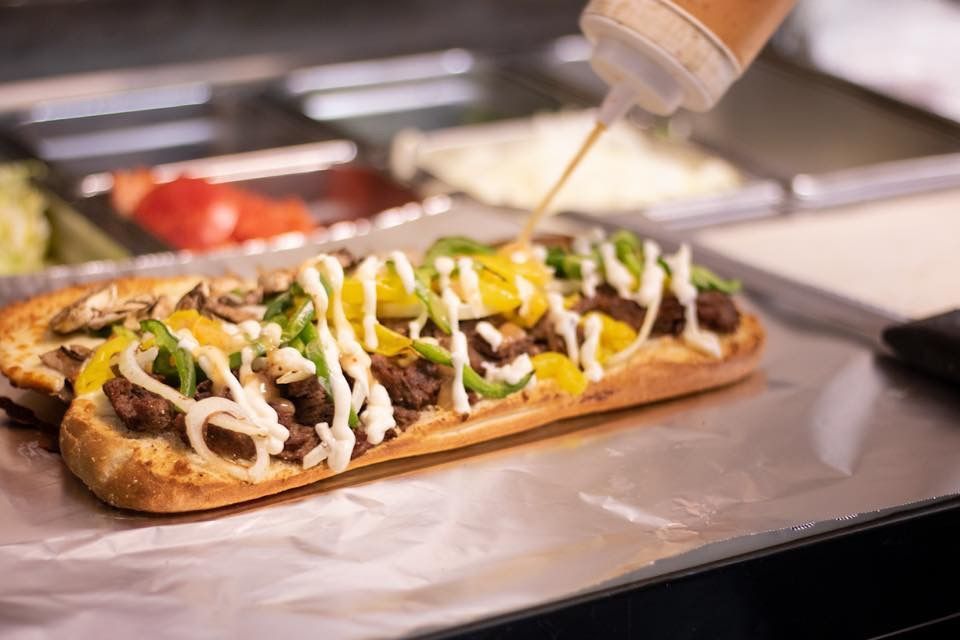 a long sub sandwich with meat, cheese, peppers, and mayonnaise being poured on it