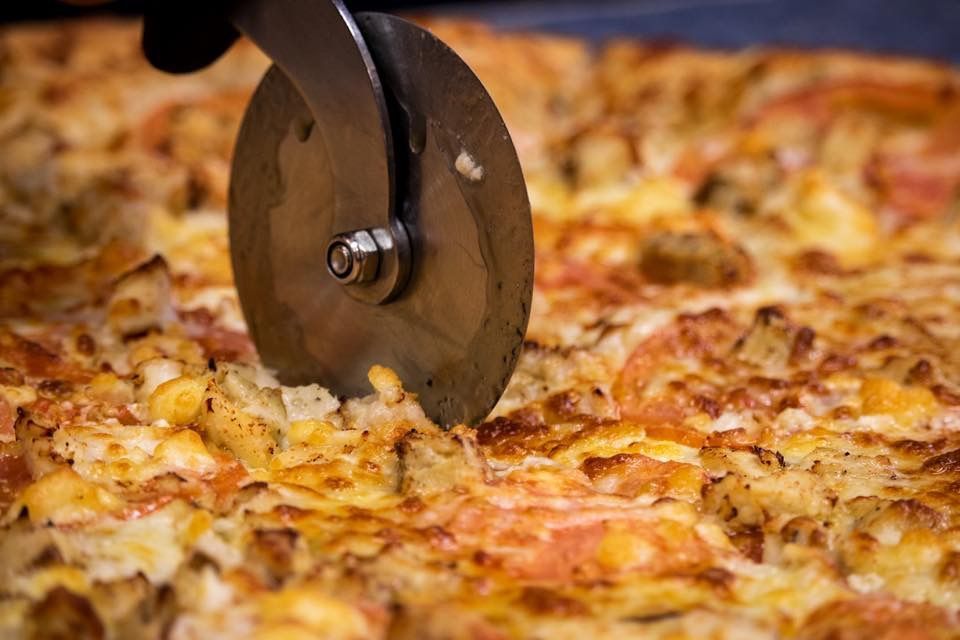 a person is cutting a pizza with a pizza cutter