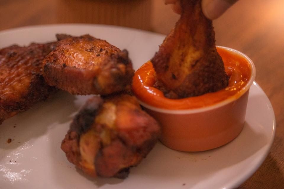 a person is dipping a chicken wing into a bowl of sauce