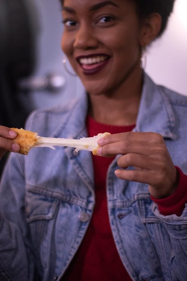 a woman in a denim jacket is eating a piece of cheese