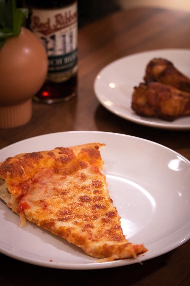 a slice of pizza is on a white plate next to a bottle of beer