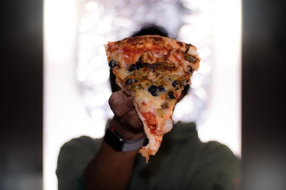 a man is holding a slice of pizza in front of his face