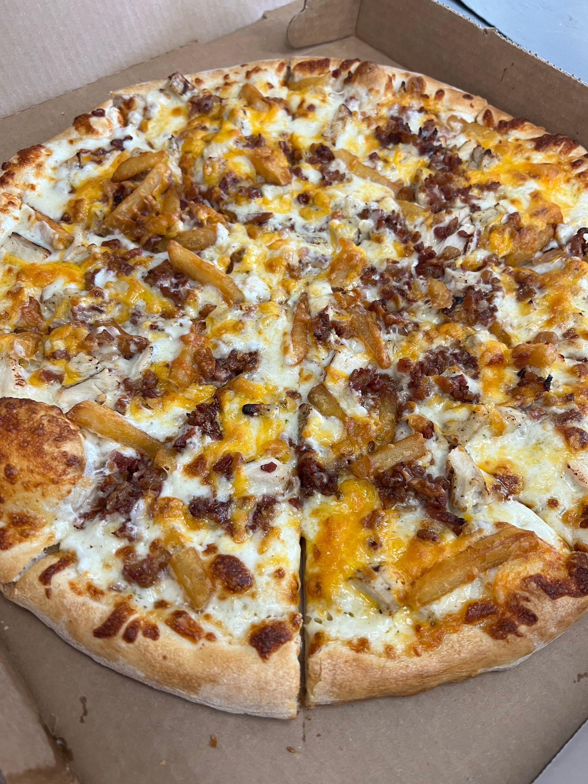 a pizza with french fries and bacon on it is in a box