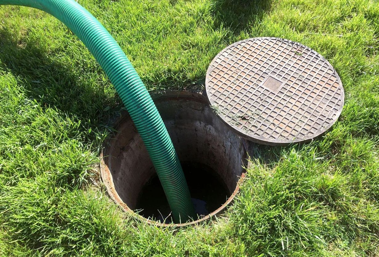 Green hose in open ground hole beside a metal manhole cover on grass