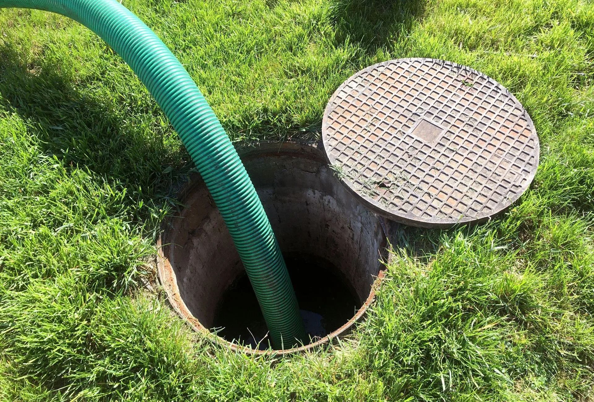 Green hose in open ground hole beside a metal manhole cover on grass
