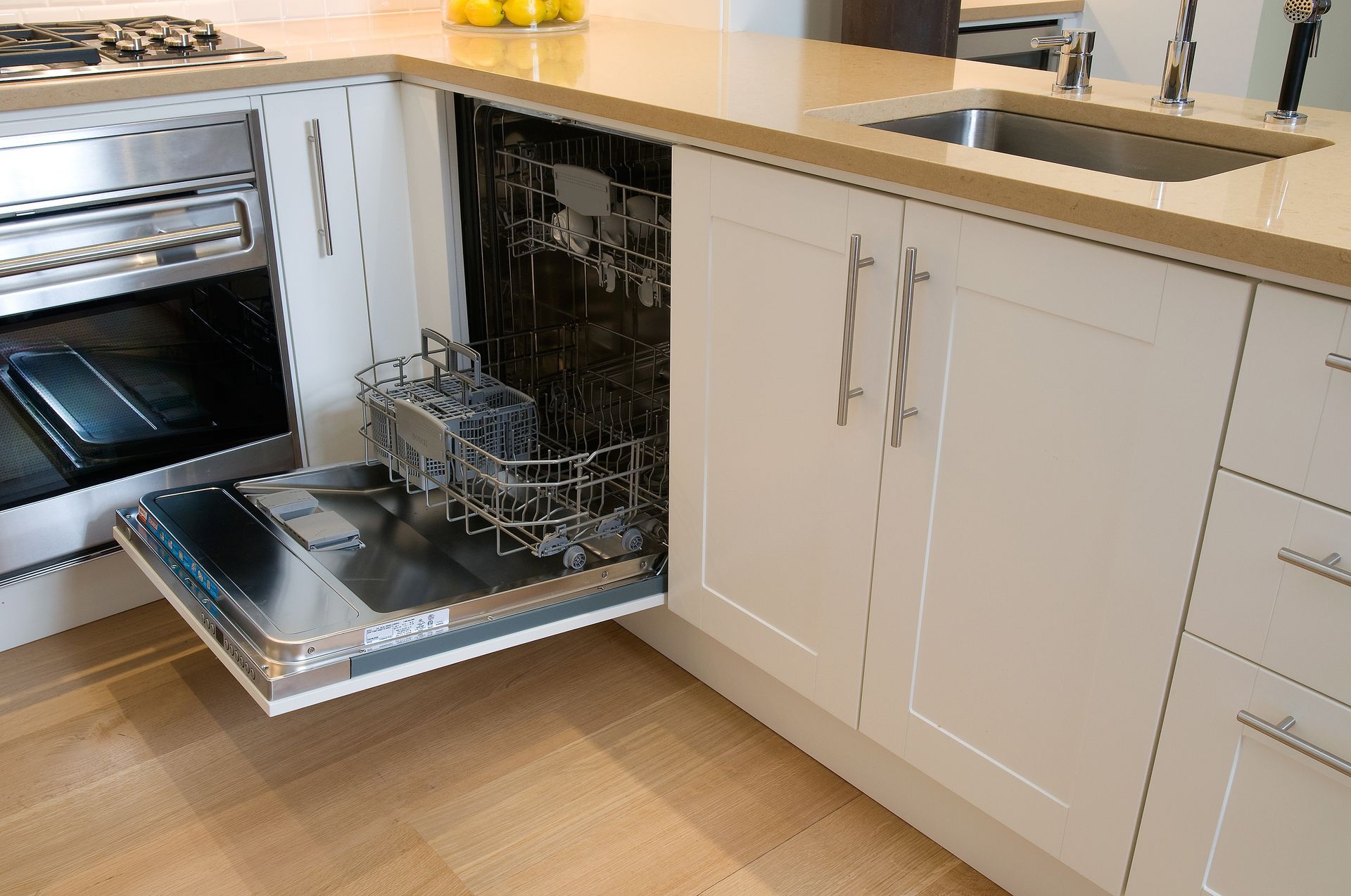 Open dishwasher with dishes in a modern kitchen beside white cabinets and a built-in oven