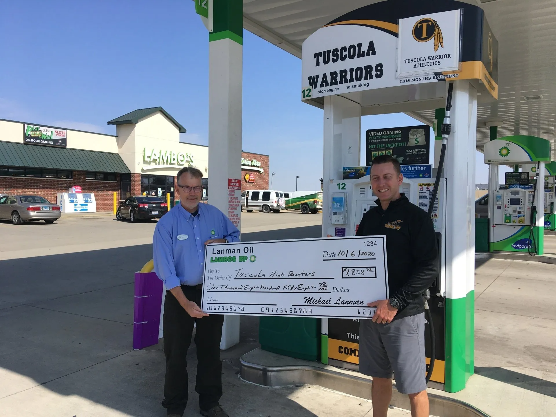 Two men are holding a large check in front of Lambo's gas station.