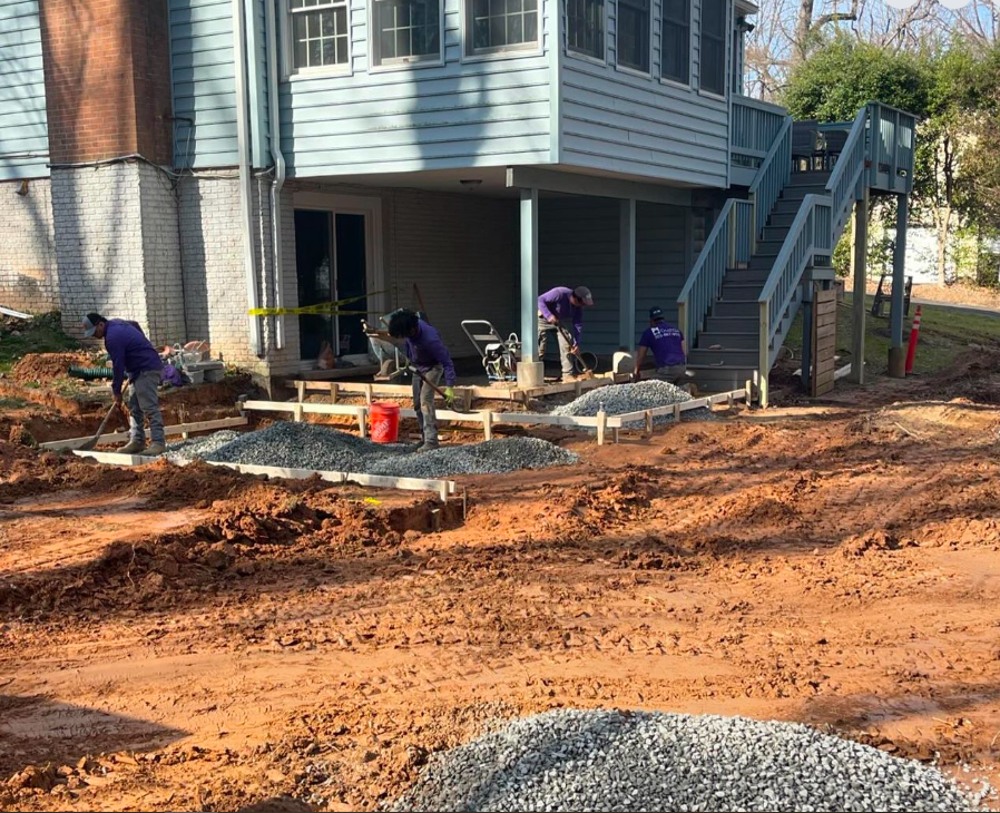 A group of construction workers are working on a driveway in front of a house.