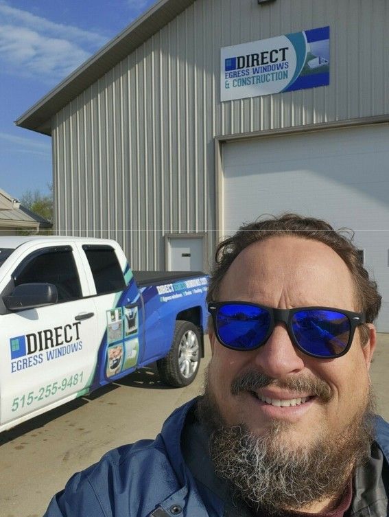 Man in sunglasses smiles in front of a blue and white Direct Egress Windows truck and building.