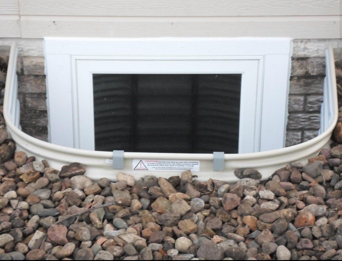 Exterior view of a building with multiple basement window wells along the foundation. Construction site.